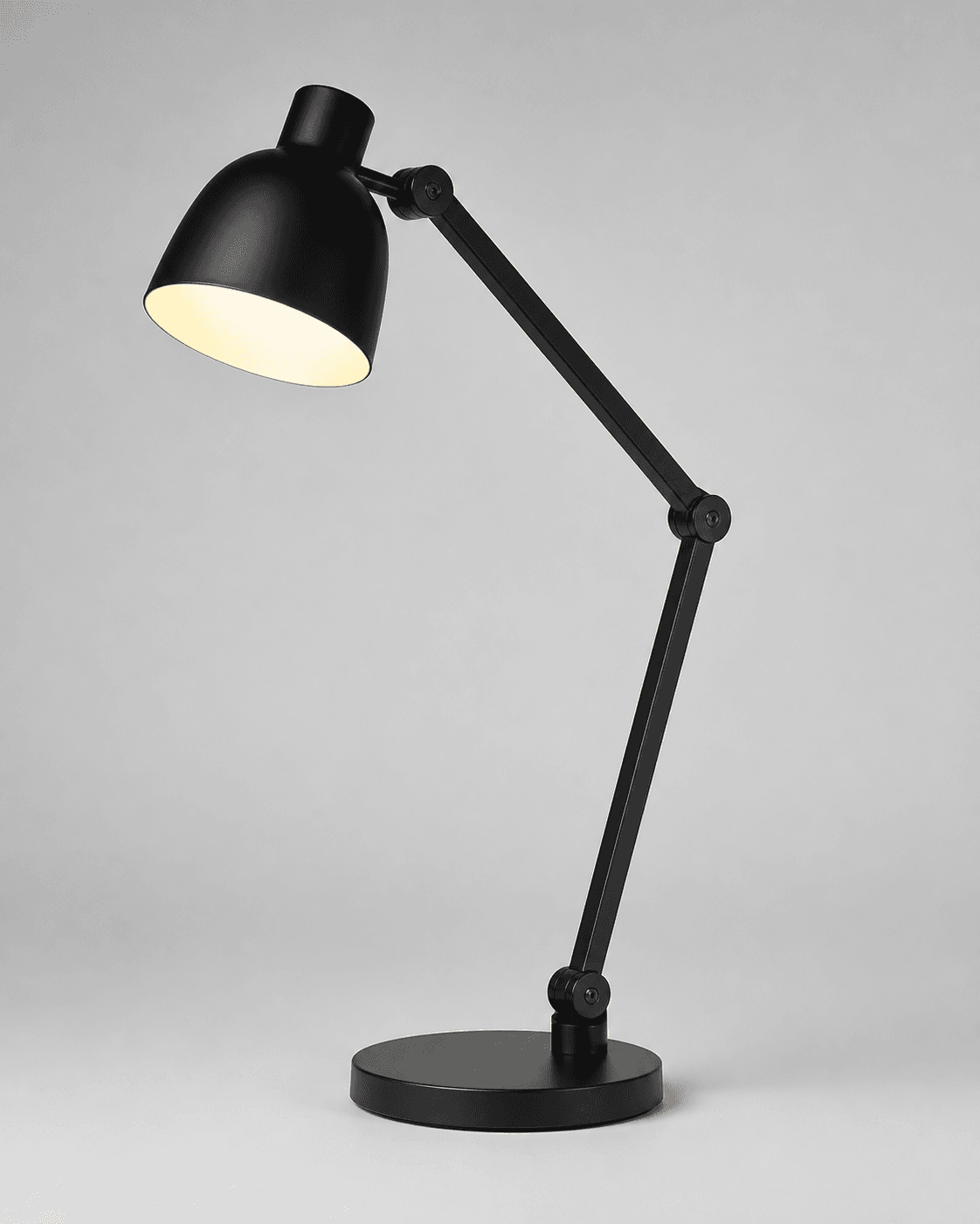 Black adjustable desk lamp with a warm-lit rounded shade, articulated stem, visible hinge joints, control area, and round base on a neutral gray background
