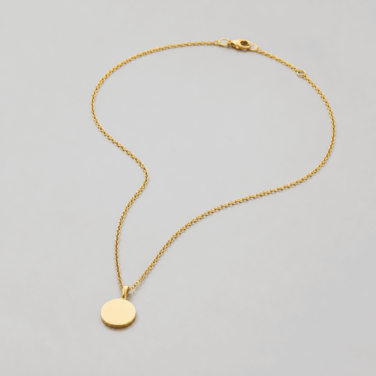 Simple pendant necklace with a round pendant, fine chain, and clasp on a neutral surface