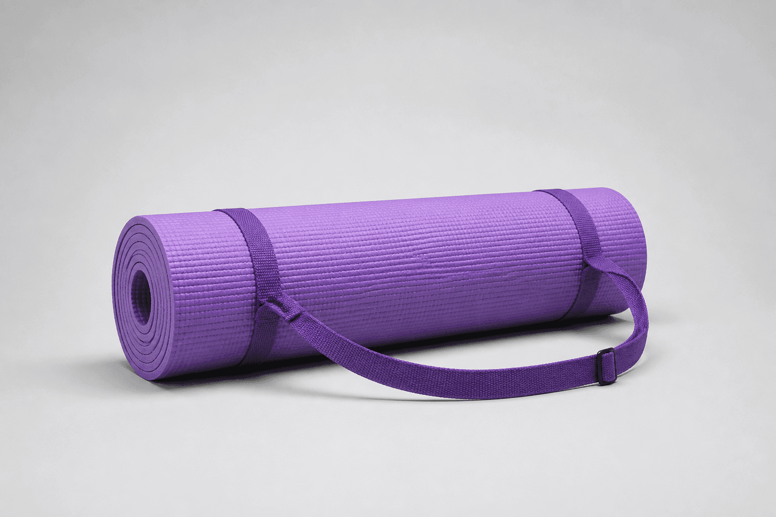 Purple rolled exercise mat with a ridged surface, two straps, a buckle, and a visible rolled edge on a neutral background